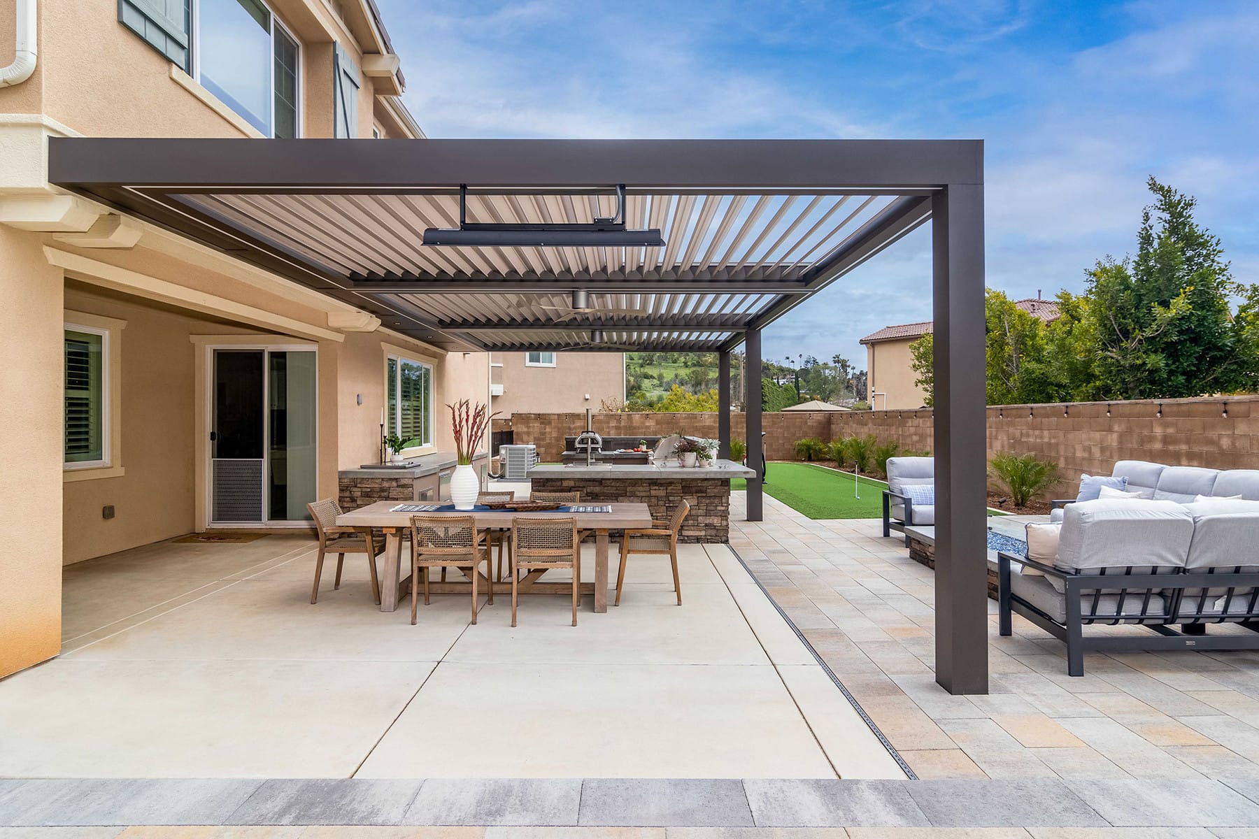 Open slat Outdoor Elements louvered pergola with integrated lightining covering a backyard dining area and kitchen.
