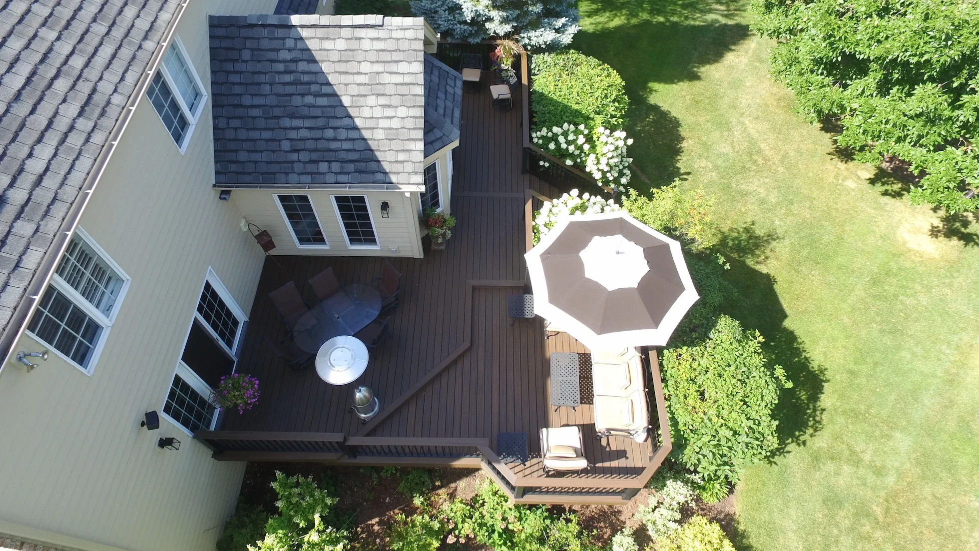 Backyard outdoor living space in Naperville, IL, featuring a Trex Enhance® composite deck in Toasted Sand color, patio dining furniture, and lush landscaping.