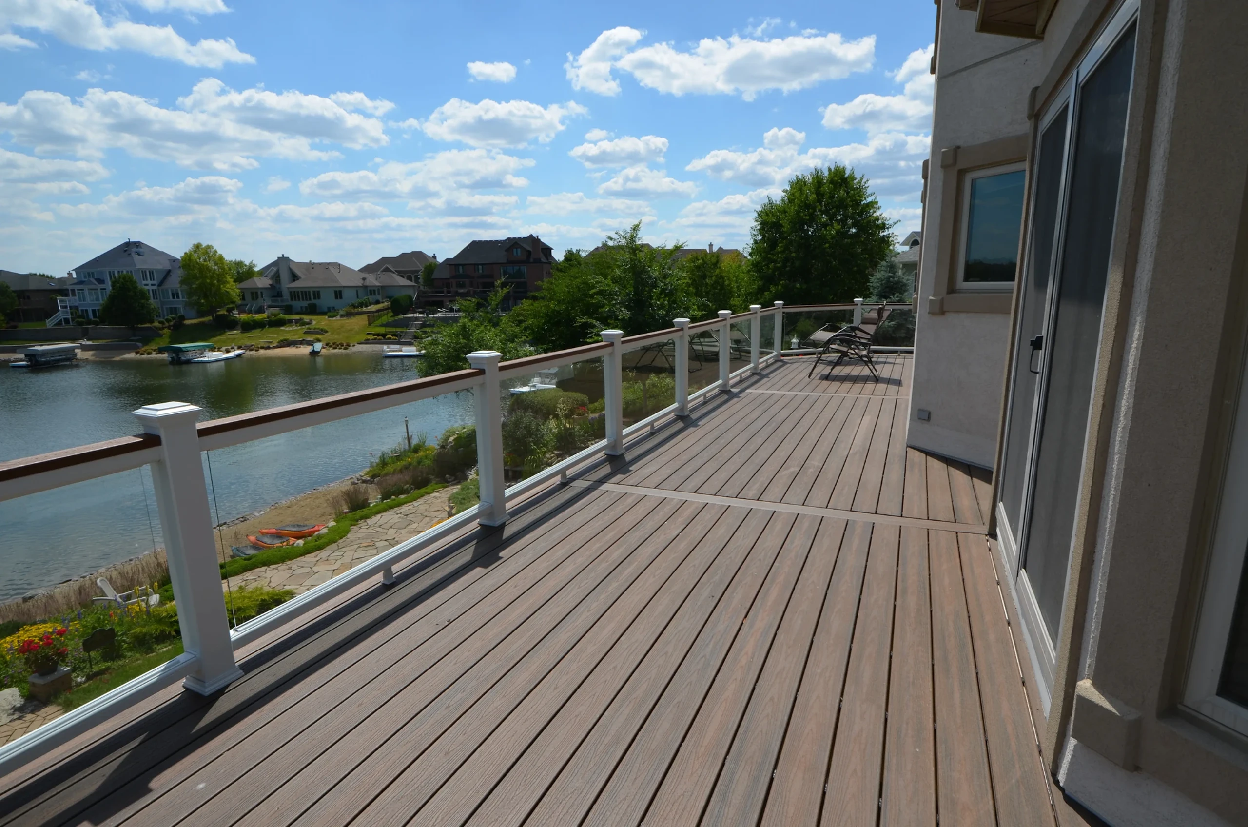 Perspective view from a balcony of an elevated Trex Select® Saddle composite deck, with Trex Signature frameless glass infill railings, overlooking a scenic lakeside in Naperville, IL.