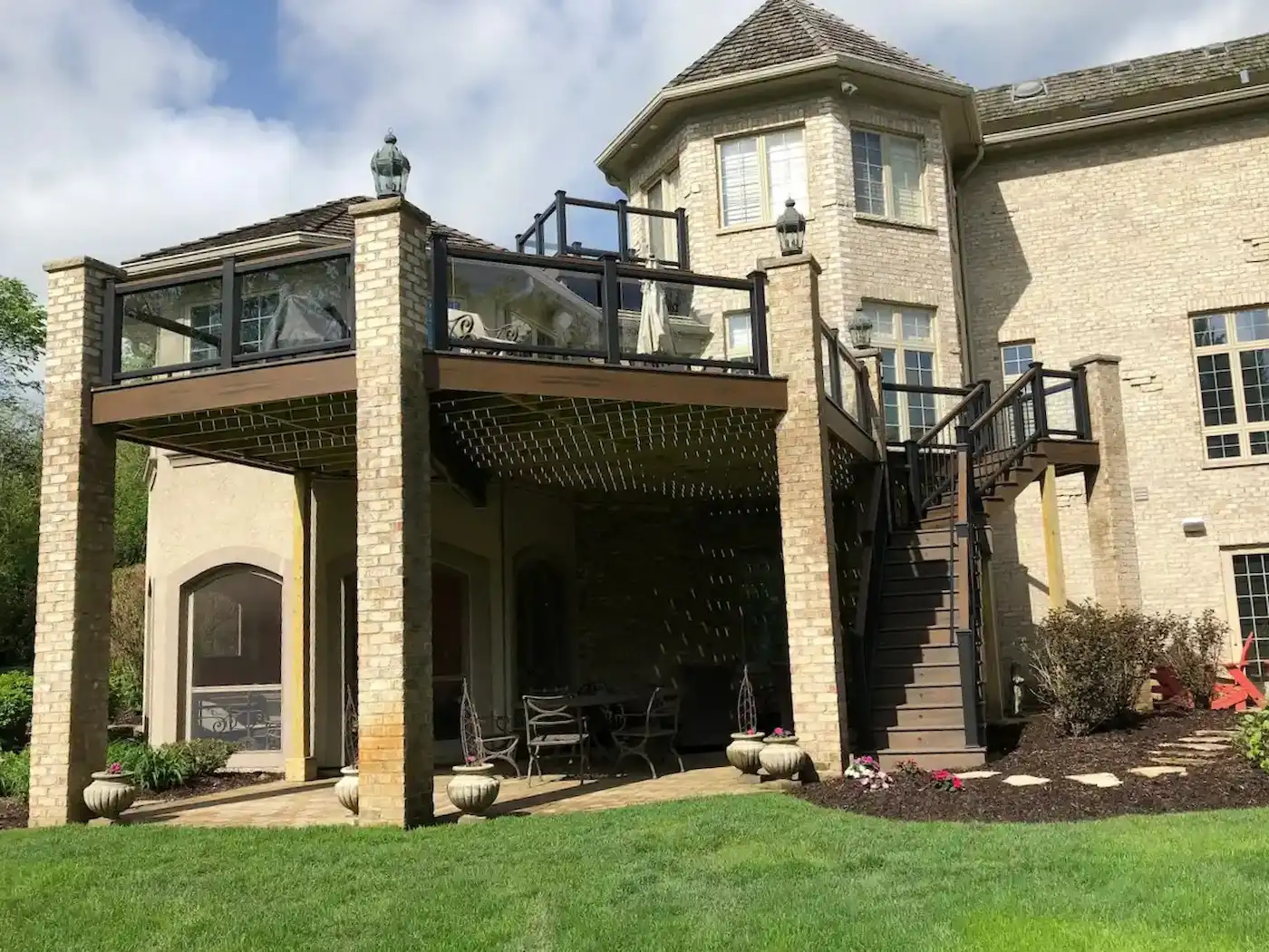 Newly built raised Trex deck with an angled staircase, glass infill railings, and brick pillar supports in the Chicago suburbs.